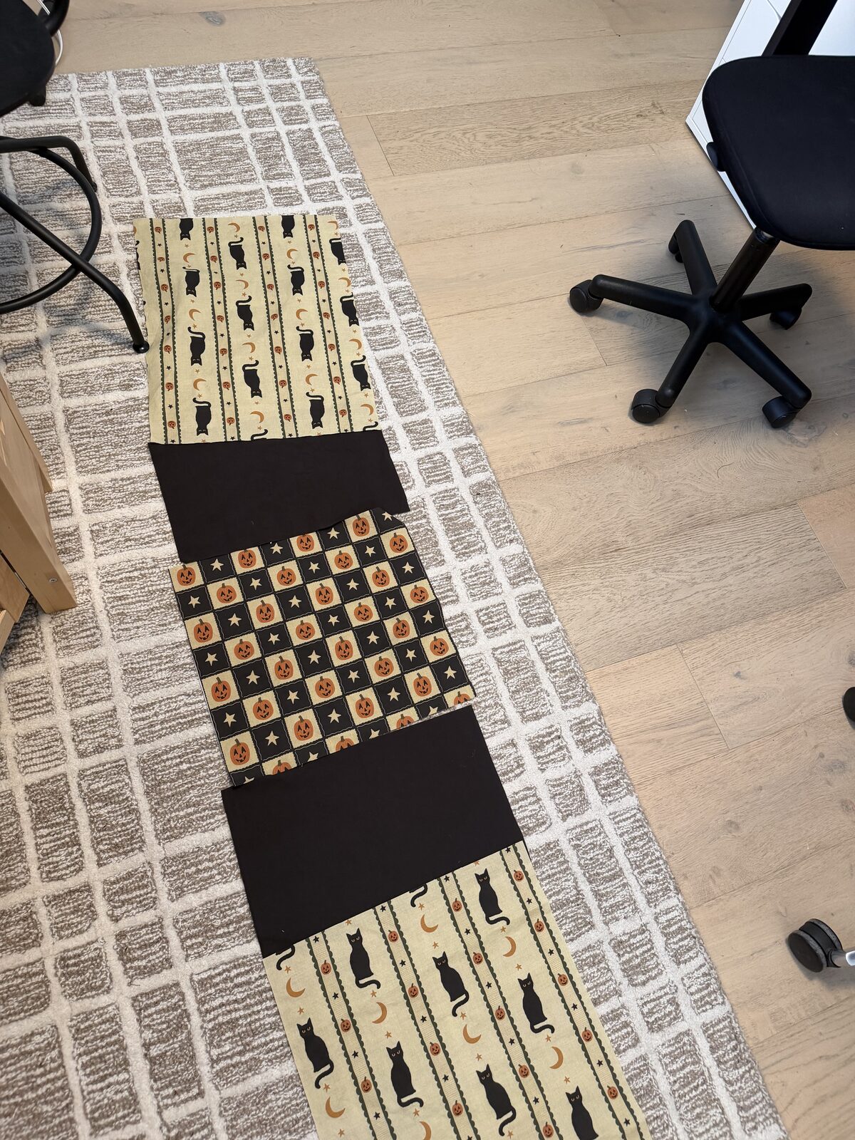 The cut blocks laid out on the floor in order: cat print, black, jack o'lantern print, black, cat print